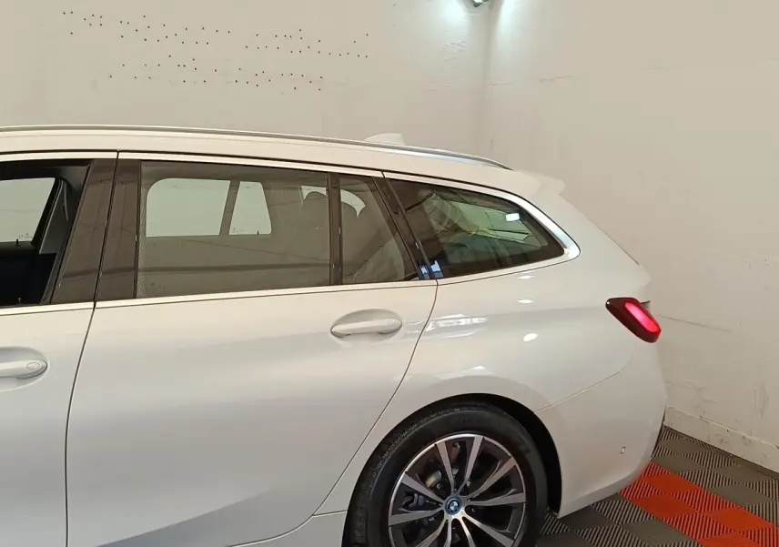 Vue latérale droite d'une BMW Série 3 Touring hybride blanche avec feux arrière allumés dans un garage.