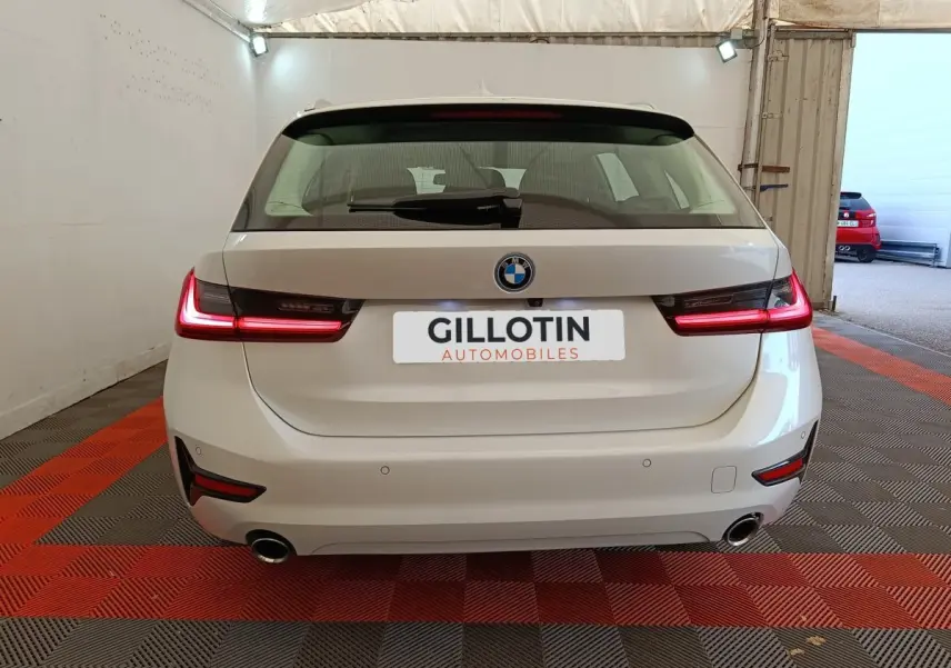 Vue arrière d'une BMW Série 3 320e blanche avec feux LED allumés, double sortie d'échappement et logo BMW visible.