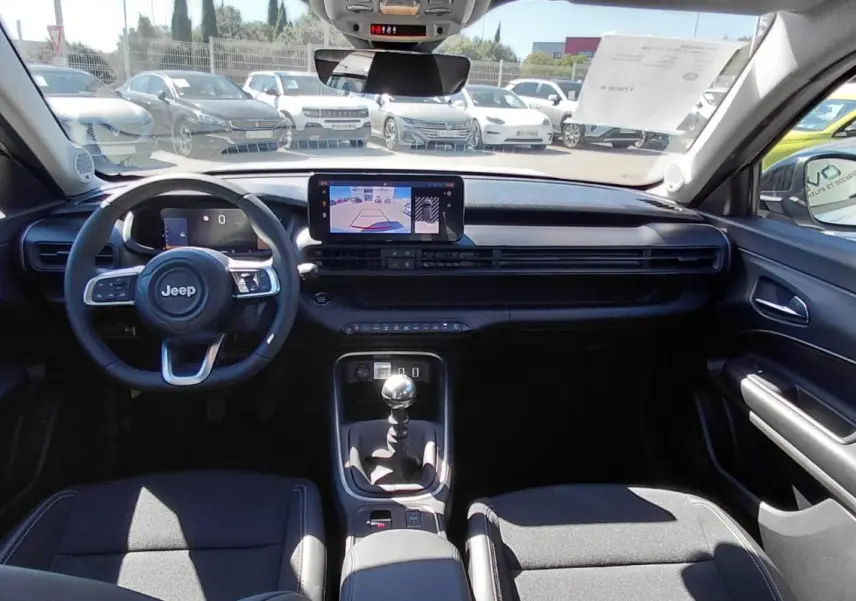 Vue intérieure frontale du Jeep Avenger 2025, tableau de bord noir avec écran tactile et levier de vitesse manuel visible.