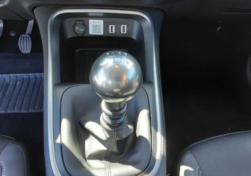 Le levier de vitesses manuel noir du Jeep Avenger blanc 2025, vu de dessus avec pédales et sièges partiels.