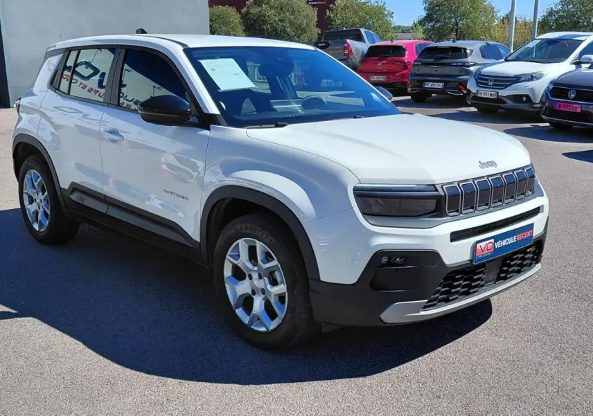 Jeep Avenger blanc en 3/4 avant droit, avec calandre distinctive et jantes alu, stationné en extérieur.