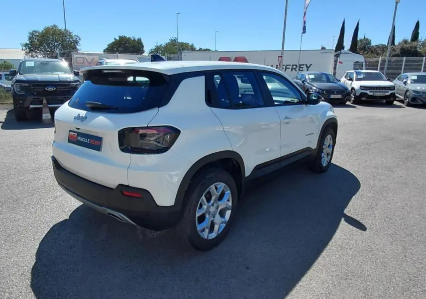 Jeep Avenger blanc vu en 3/4 arrière droit, avec feux arrière fumés et jantes alliage, stationné en extérieur.