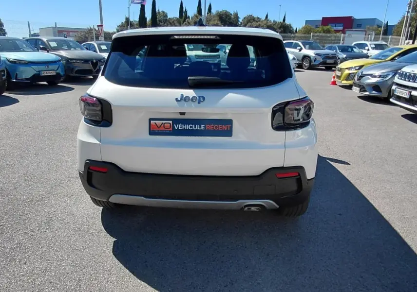Vue arrière d'un Jeep Avenger blanc 2025 avec feux arrière noirs et pare-chocs noir dans un parking extérieur.