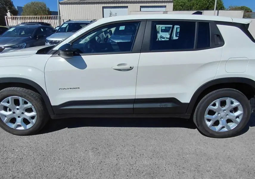 Jeep Avenger blanc vu de profil côté gauche, avec jantes alu et protections noires sur les bas de caisse.