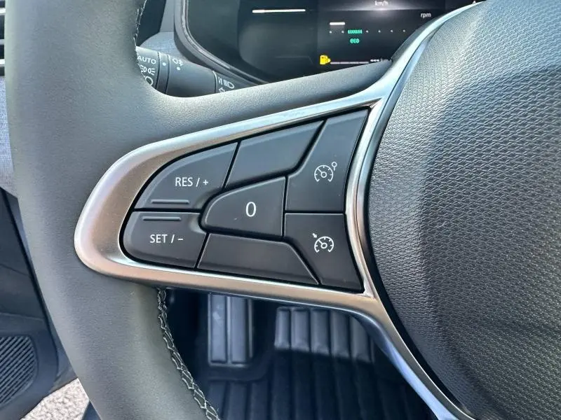 Gros plan sur les commandes de régulateur de vitesse au volant d'une Renault Clio gris Rafale, intérieur noir.