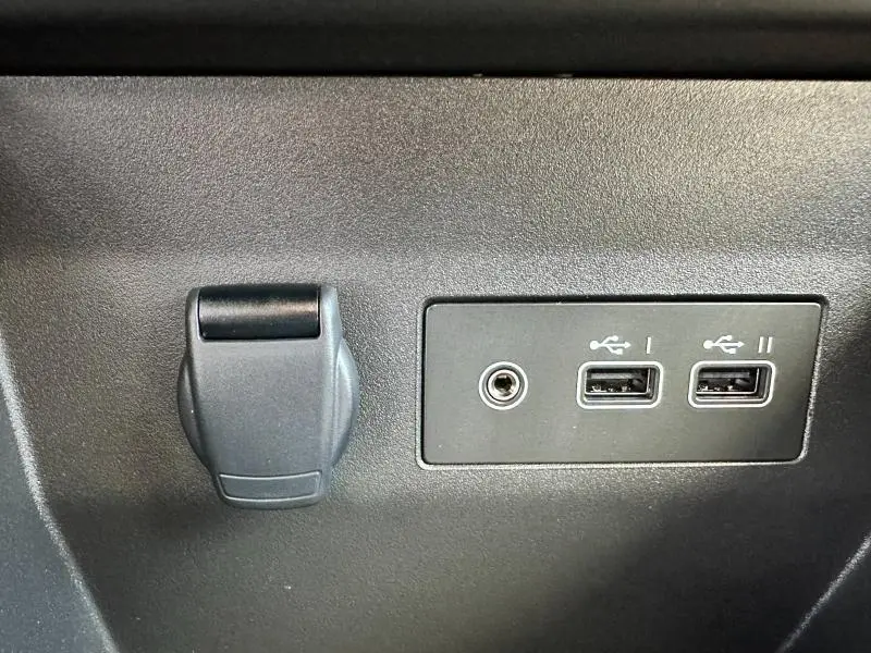 Gros plan sur la prise 12V et les deux ports USB noirs intégrés dans le tableau de bord gris d'une Renault Clio 2025.