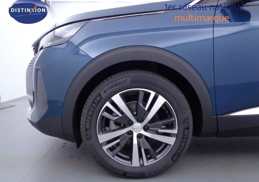 Gros plan sur la roue avant gauche d'un Peugeot 3008 2023 bleu Celebes métal avec jante alliage bicolore.