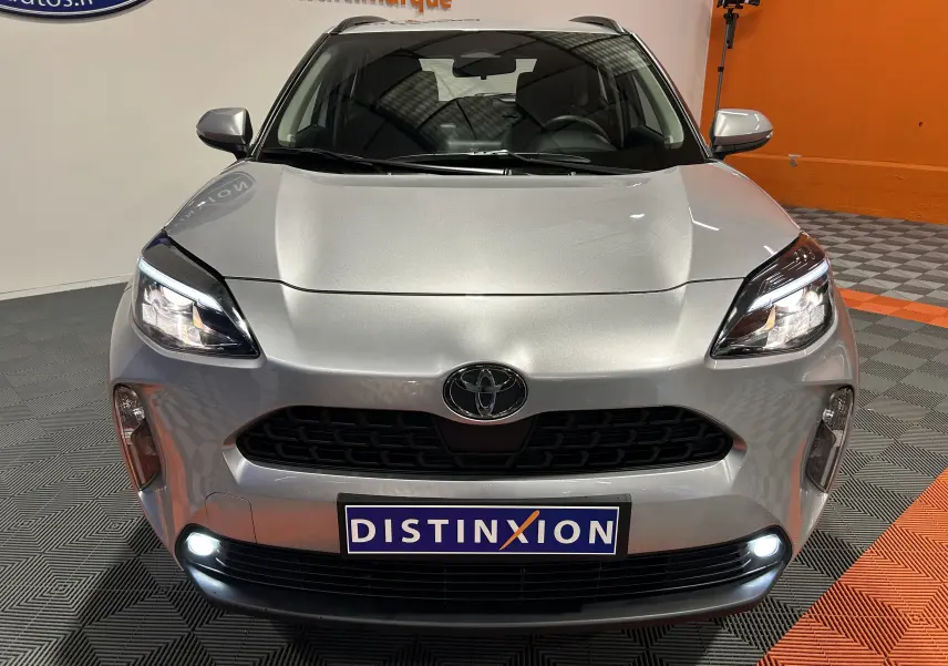 Vue frontale d'une Toyota Yaris Cross gris minéral avec phares et feux de jour allumés dans un showroom.