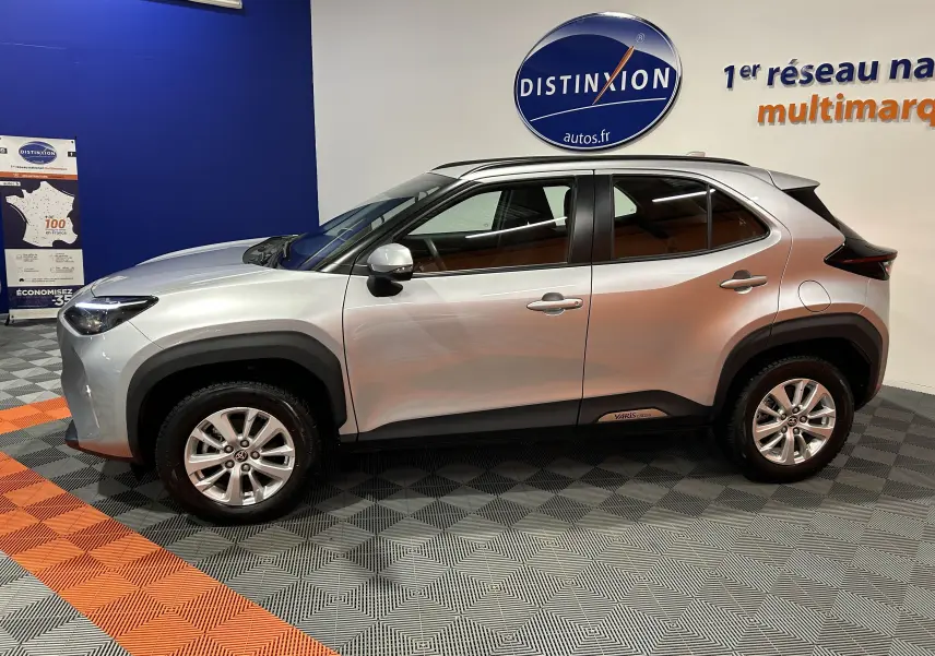 Vue de profil côté gauche d'une Toyota Yaris Cross gris minéral, avec jantes alliage et protections noires sur les passages de roues.