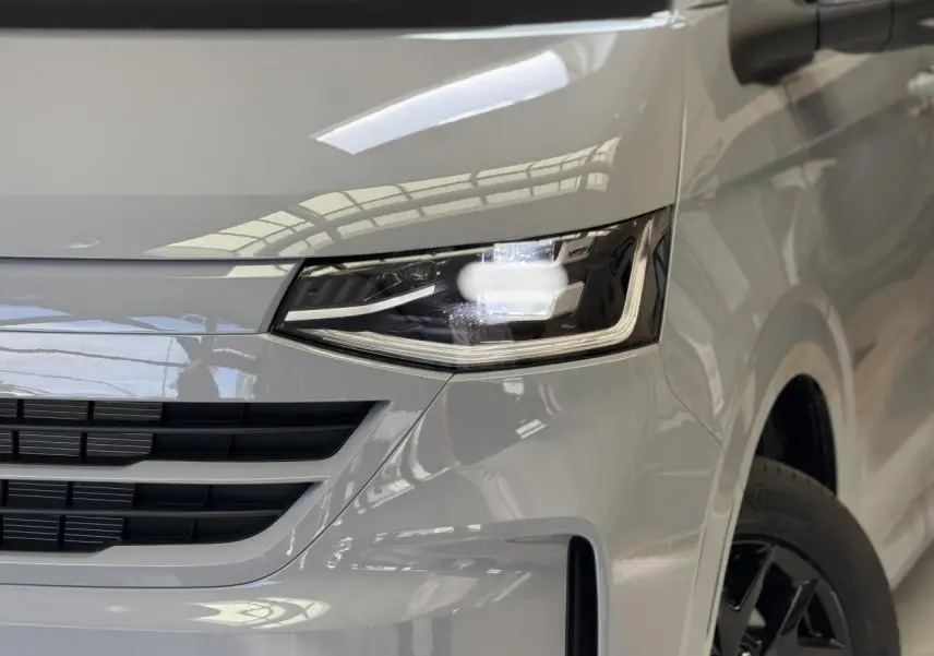 Gros plan sur l'avant droit du Volkswagen Transporter T7 gris Stone, avec phare LED Matrix et jante alliage noir brillant.