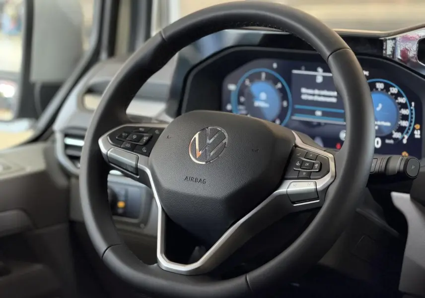 Vue rapprochée du volant multifonction noir du Volkswagen Transporter T7 avec tableau de bord digital en arrière-plan.