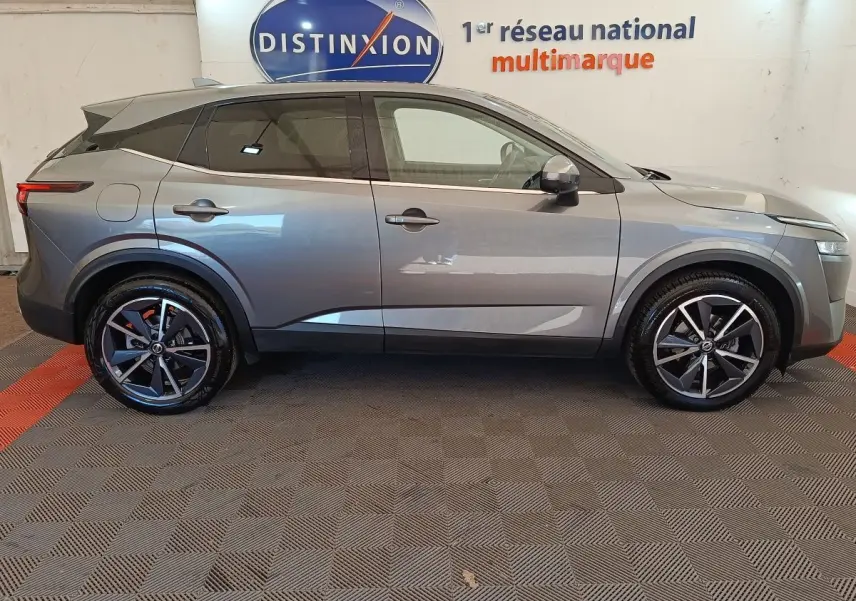 Vue de profil côté gauche d'un Nissan Qashqai gris foncé avec jantes alliage et toit noir en intérieur showroom.