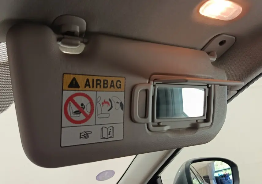 Détail du pare-soleil côté conducteur avec miroir intégré et étiquette d’avertissement airbag dans un Nissan Qashqai gris foncé.