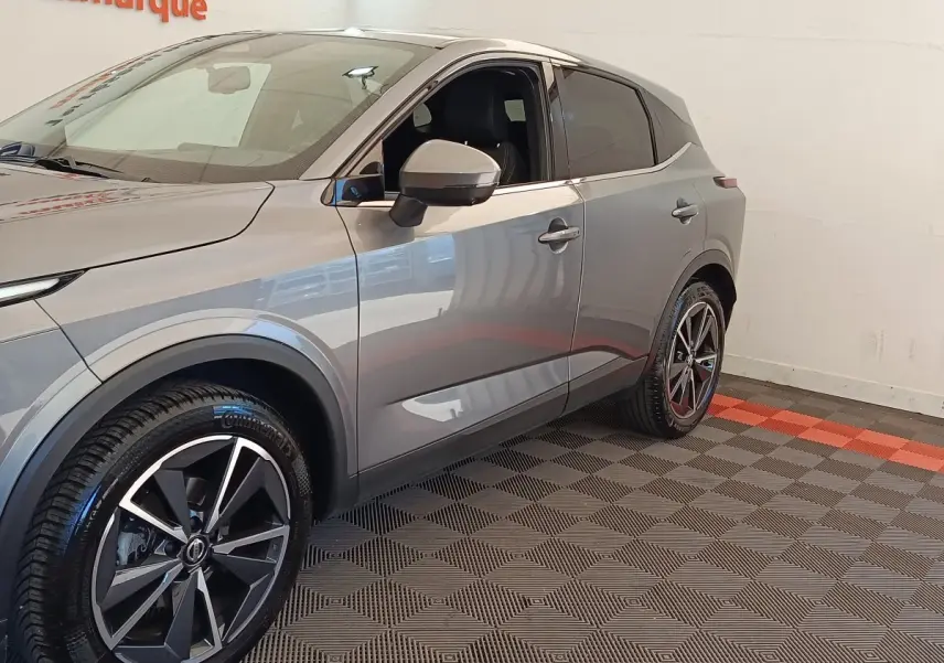Vue 3/4 avant droit du Nissan Qashqai gris foncé avec jantes alliage noires et grises, intérieur visible côté conducteur.