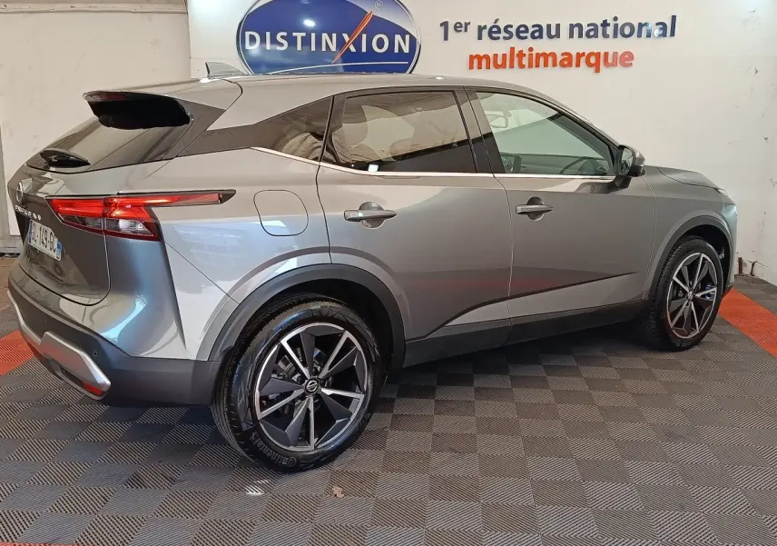 Vue 3/4 arrière droite d’un Nissan Qashqai gris foncé avec jantes alliage et feux arrière LED, en intérieur showroom.