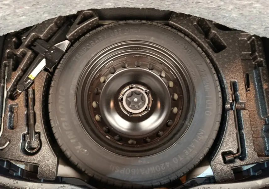 Vue rapprochée de la roue de secours noire et des outils de changement de pneu dans le coffre d’un Nissan Qashqai gris foncé.