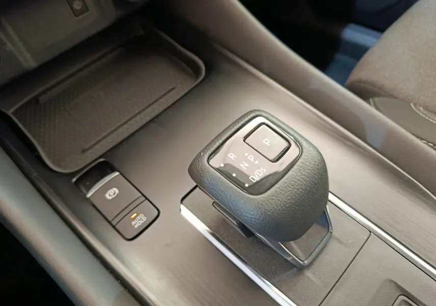 Gros plan sur la commande de boîte automatique noire et le bouton frein à main électrique du Nissan Qashqai gris foncé, intérieur.