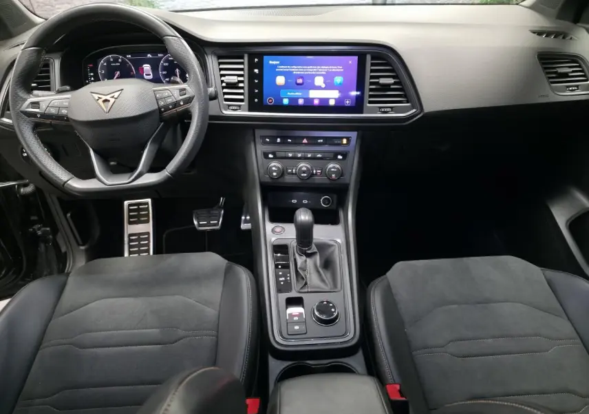 Vue intérieure centrée du tableau de bord et console centrale du CUPRA Ateca 2024 avec volant sport et sièges en suédine noir.