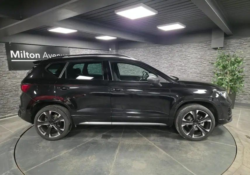 Vue de profil côté gauche d’un CUPRA Ateca noir brillant avec jantes alliage 19 pouces dans un showroom intérieur.