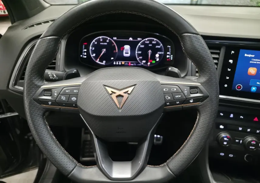 Vue rapprochée du volant sport en cuir perforé noir avec logo CUPRA cuivre et tableau de bord numérique.