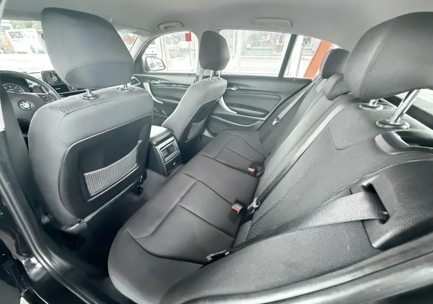 Vue intérieure arrière de la BMW Série 1 noire, montrant les sièges arrière en tissu noir et les dossiers des sièges avant.