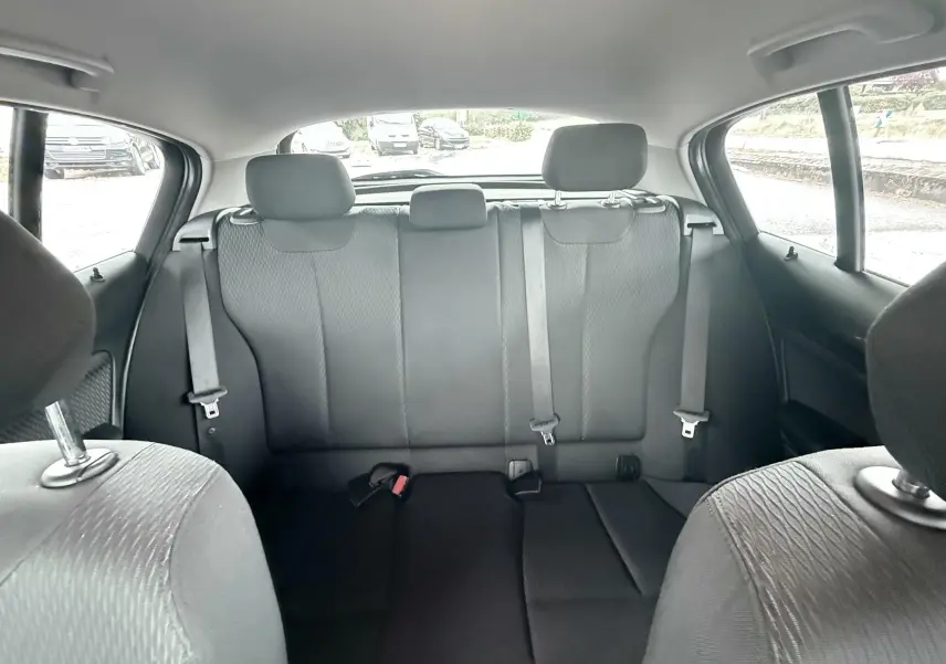 Vue intérieure arrière de la BMW Série 1 noire, montrant les sièges arrière en tissu noir avec ceintures de sécurité.