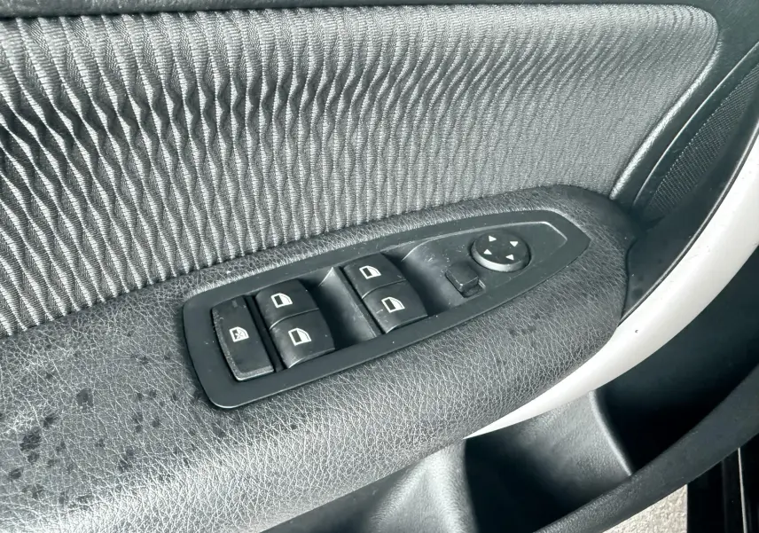 Gros plan sur les commandes de lève-vitres et réglage des rétroviseurs sur la porte côté conducteur d'une BMW Série 1 noire.