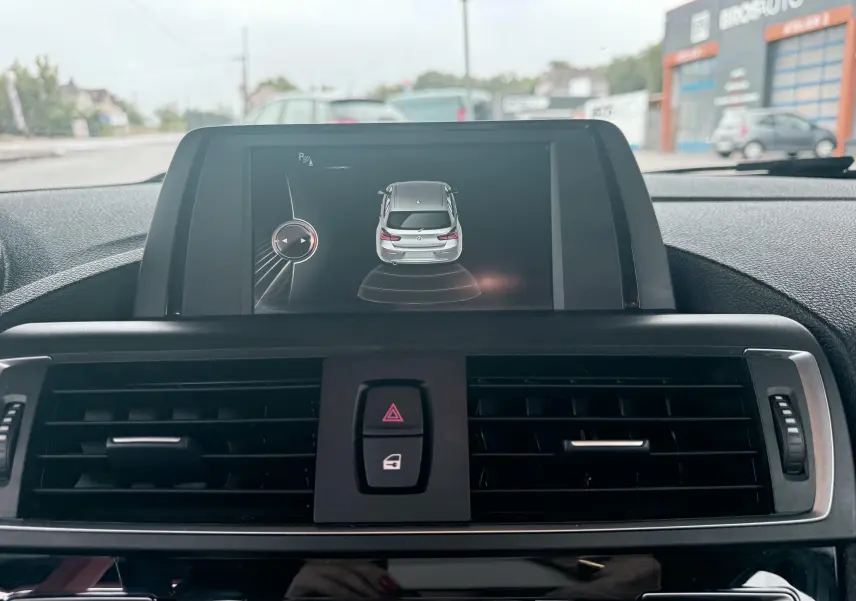 Vue intérieure centrée sur l'écran multimédia affichant l'aide au stationnement de la BMW Série 1 noire de 2016.