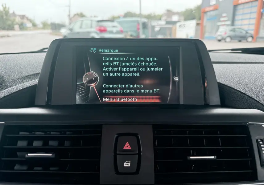 Vue intérieure centrée sur l'écran multimédia affichant un message Bluetooth dans une BMW Série 1 noire de 2016.