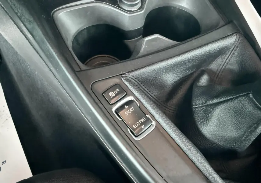 Gros plan sur la console centrale de la BMW Série 1 noire, montrant le levier de vitesses manuel et les boutons modes Sport et Eco Pro.