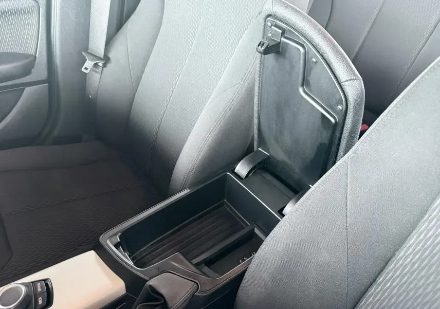 Vue intérieure rapprochée du rangement central ouvert entre les sièges avant en tissu noir d’une BMW Série 1 2016.