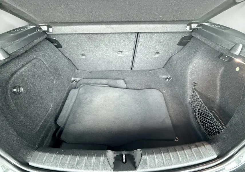 Coffre ouvert de BMW Série 1 noire, vue plongeante montrant l’espace de rangement et tapis intérieur gris.