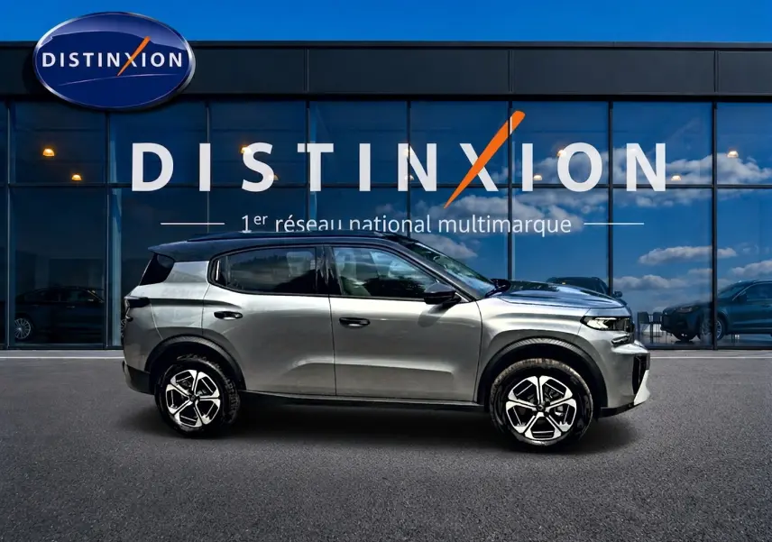 Vue de profil côté gauche d'un Citroën C3 Aircross gris mercury devant une vitrine Distinxion.