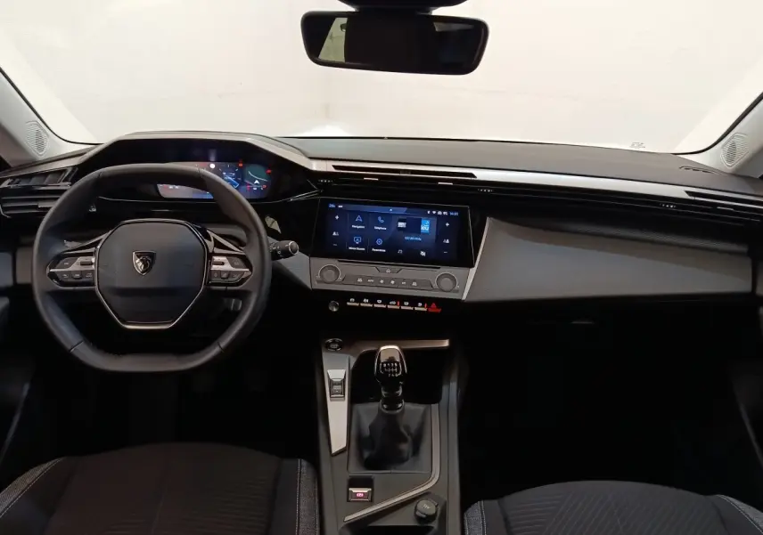 Vue intérieure frontale du poste de conduite de la Peugeot 308 blanche, avec volant cuir et écran tactile central.