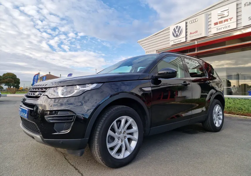Profil côté gauche d'un Land Rover Discovery Sport Mark II noir, version TD4 150 SE A, stationné devant un garage multimarques.