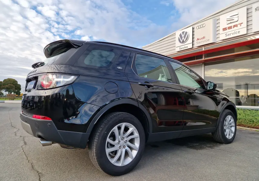 Vue 3/4 arrière droite d'un Land Rover Discovery Sport Mark II noir, avec jantes argentées, stationné devant un bâtiment moderne.