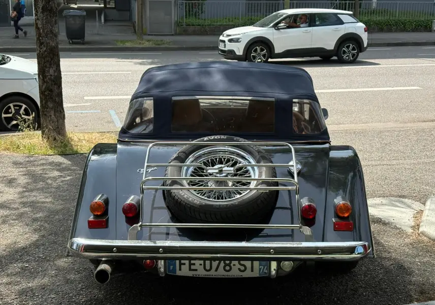 Vue arrière d'une Morgan Plus 4 1995 bleu foncé avec capote noire et roue de secours sur porte-bagages chromé.