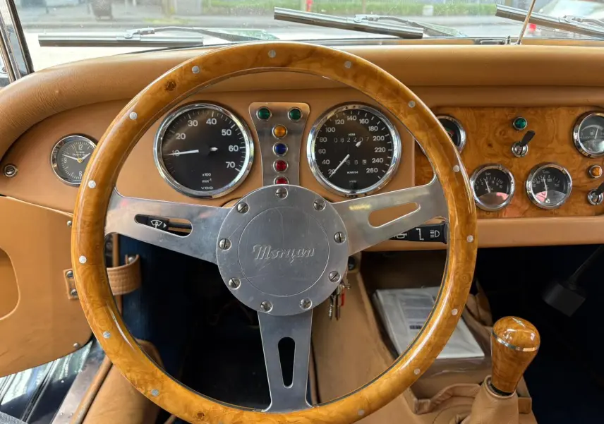 Vue intérieure centrée sur le volant en bois et le tableau de bord en bois clair d'une Morgan Plus 4 bleu foncé de 1995.