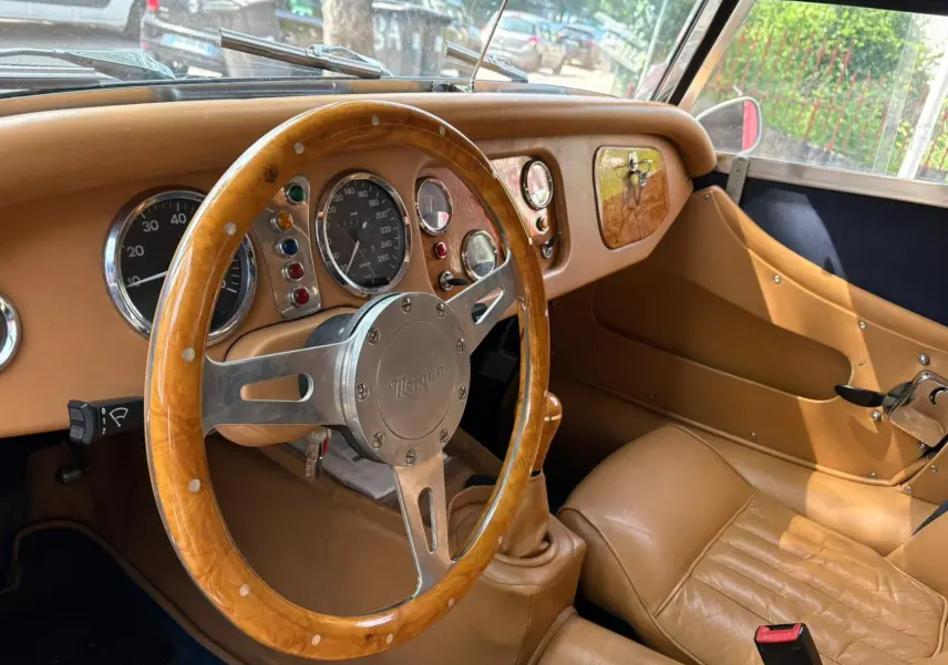 Intérieur beige avec volant en bois et tableau de bord rétro de la Morgan Plus 4 1995, vue côté conducteur.