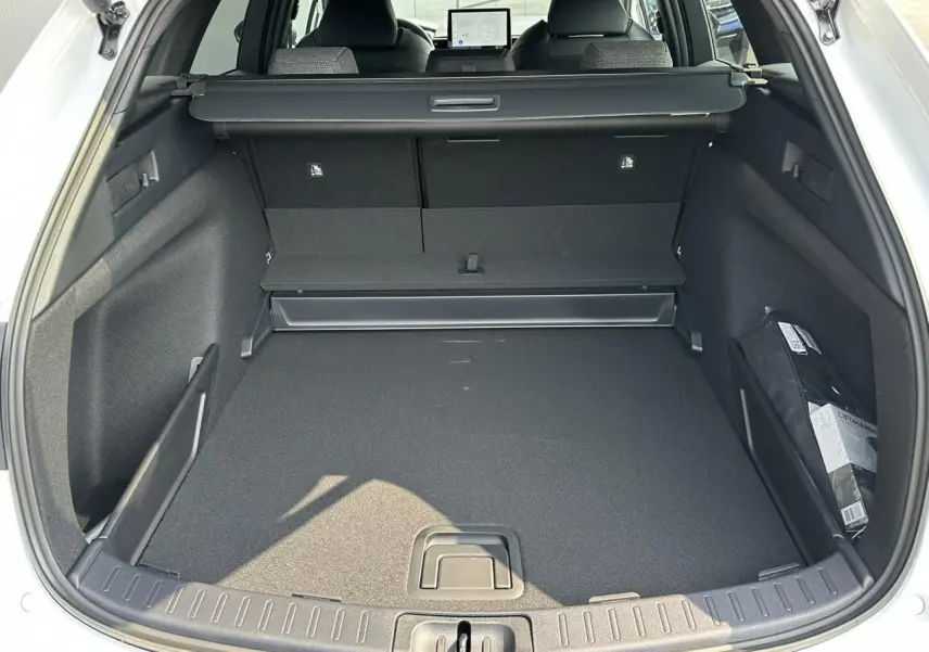 Coffre ouvert vu de l'arrière d'une Toyota Corolla Touring Sport 1.8 Hybrid blanc neige, intérieur noir spacieux.