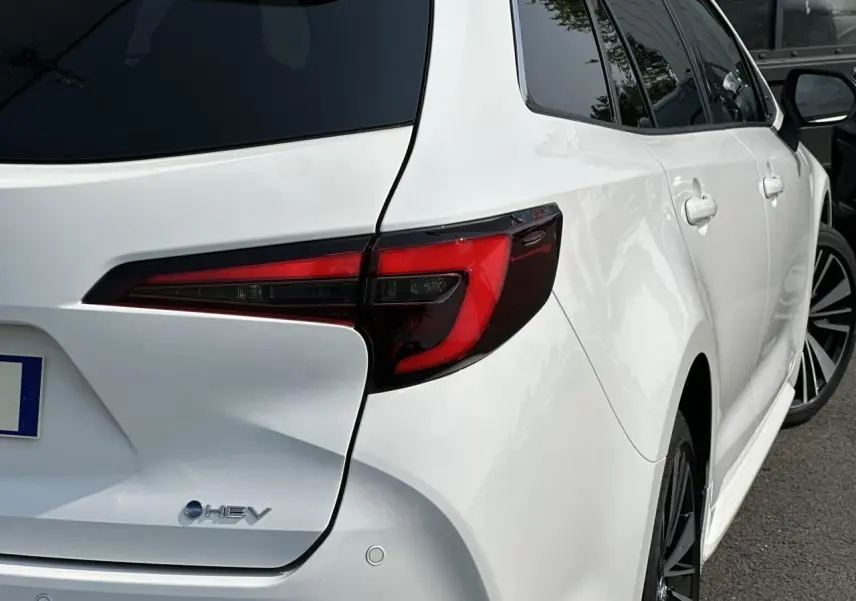 Vue 3/4 arrière droite d'une Toyota Corolla Touring Sport blanche Neige avec feux arrière LED et jantes alliage noires.