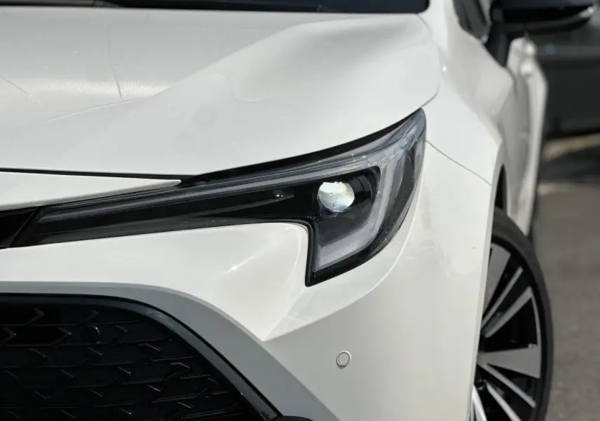 Gros plan sur le phare avant droit blanc neige de la Toyota Corolla Touring Sport 2025 avec jante alliage noire et grise.