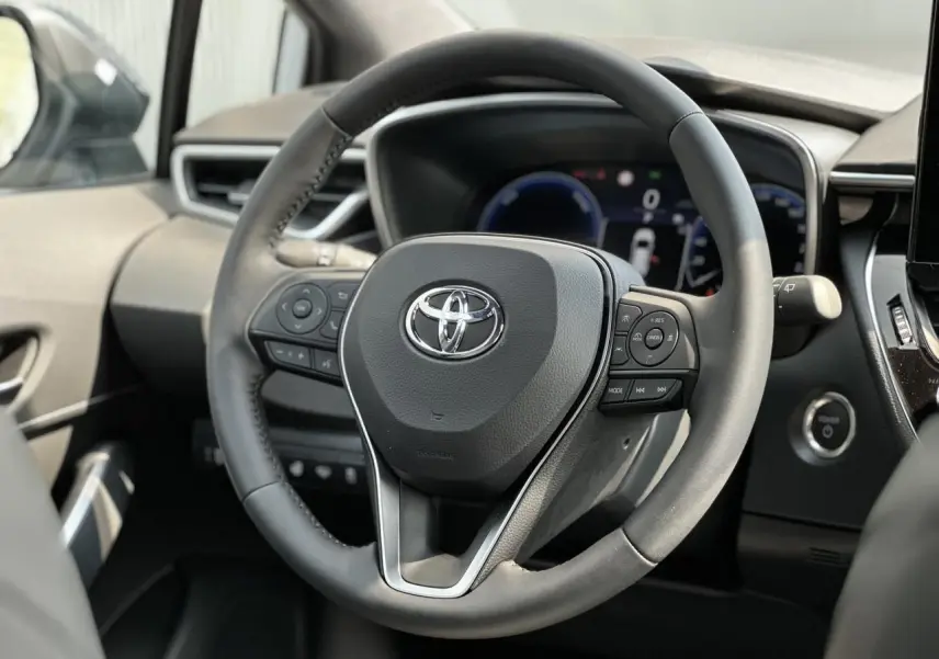 Volant multifonction noir de la Toyota Corolla Touring Sport 1.8 Hybrid 2025, vue rapprochée côté conducteur.