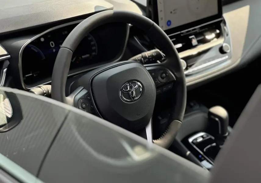 Vue rapprochée du volant multifonction noir et du tableau de bord numérique de la Toyota Corolla Touring Sport 2025.