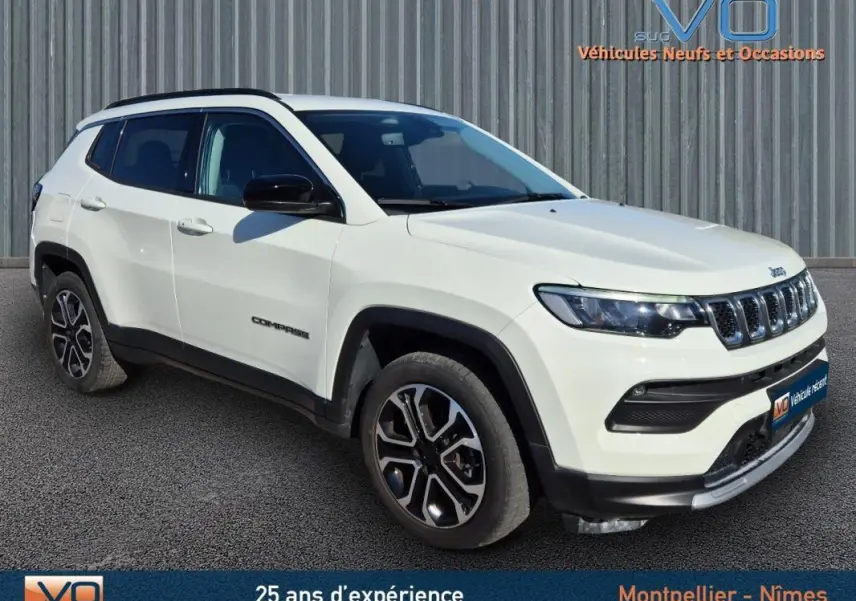 Jeep Compass blanc vue 3/4 avant droit, avec jantes 18 pouces et barres de toit noires sur fond urbain.