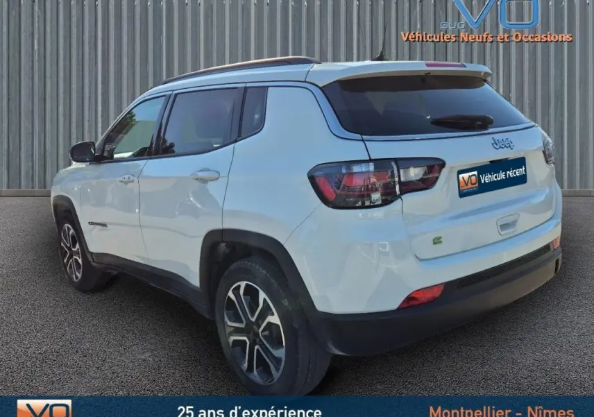 Vue 3/4 arrière gauche d'un Jeep Compass blanc 2023 avec barres de toit et jantes 18 pouces noires et argentées.