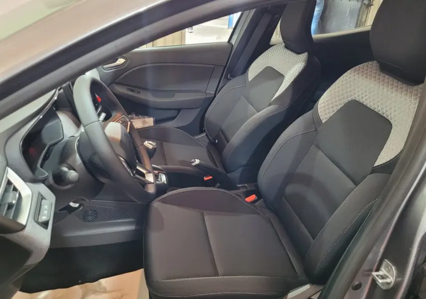 Vue intérieure côté conducteur de la Renault Clio gris foncé 2025, sièges avant en tissu bicolore et volant multifonction.