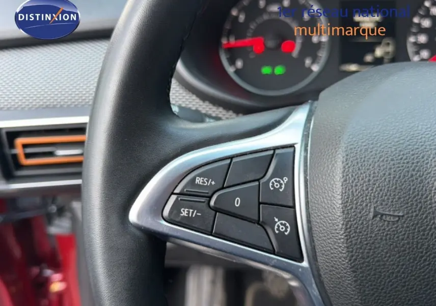 Gros plan sur le volant avec commandes de régulateur de vitesse, intérieur rouge fusion visible en arrière-plan.