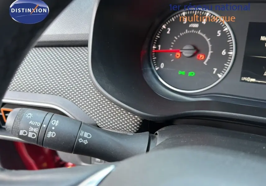 Gros plan sur le tableau de bord et le commodo gauche d’une Dacia Sandero Stepway rouge fusion, affichant le compte-tours et témoins lumineux.