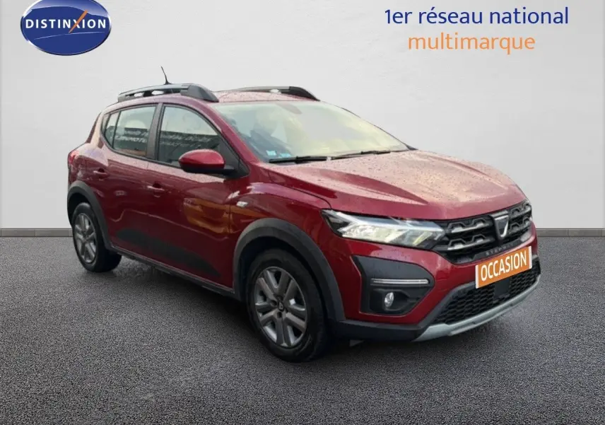 Dacia Sandero Stepway rouge fusion vue 3/4 avant gauche, avec barres de toit et protections noires.